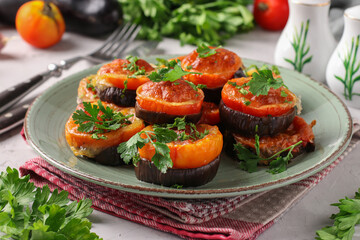 Eggplants and tomatoes baked with suluguni cheese and garlic served on a plate on light gray background