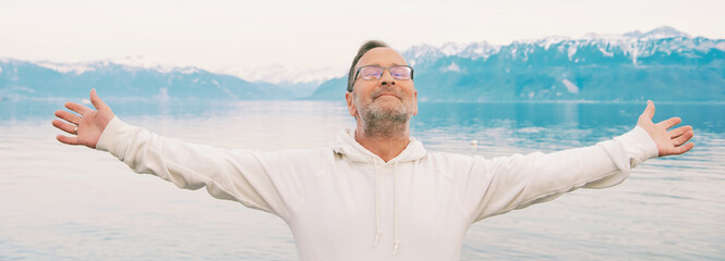 Panoramic banner with portrait of handsome man, arms wide open, meditating by the lake, wearing white sweatshirt
