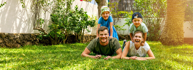 happy family with two children lying in the home backyard garden lawn and looking at camera. banner...