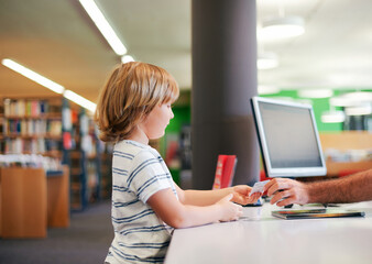 Portrait of cute little boy taking books in library, giving  membership card to librarian - 499023391