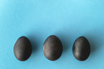 Three painted blue Easter eggs in a row on a blue background. Top view, space for text