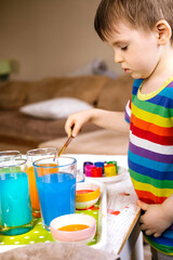 Cute baby boy learning mixing different colors with water and paint in containers. Early development