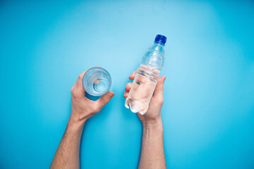 Hand holding plastic water bottle on blue background