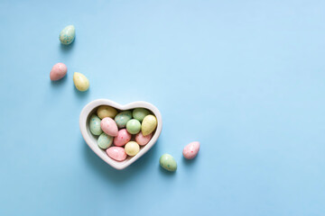 on a blue background, a heart vase with candy eggs and Easter treats are scattered nearby