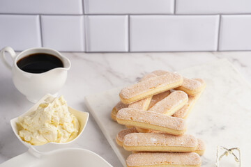 Step by step process of preparing italian dessert tiramisu out of ladyfinger biscuits, mascarpone cheese, espresso on white marble background