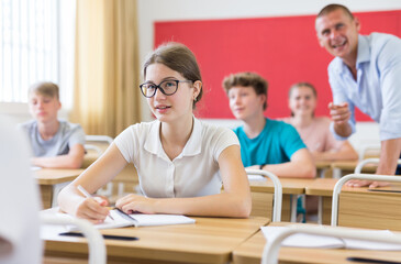 Young stunents sitting in classroom and smiling. Teacher explaining something funny.