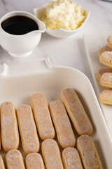 Step by step process of preparing italian dessert tiramisu out of ladyfinger biscuits, mascarpone cheese, espresso on white marble background