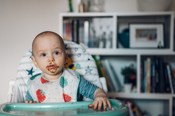 Baby boy eating chocolate while sitting in a dinning chair
