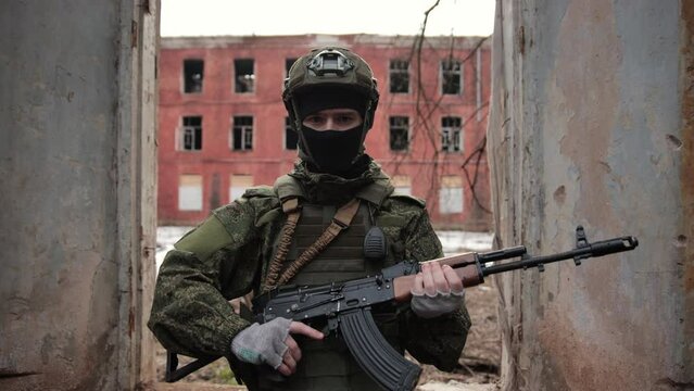 Close Up Portrait of professional fully equipped soldier with Kalashnikov assault rifle, looking into the camera in the ruins of a house destroyed by war. Ukrainian or Russian soldier. Cinematographic