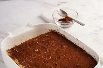 Step by step process of preparing italian dessert tiramisu out of ladyfinger biscuits, mascarpone cheese, espresso on white marble background