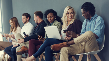 Youve been shortlisted but who will get the job. Shot of a group of businesspeople using different wireless devices while waiting in line for an interview.