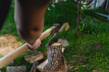 A young man is chopping wood in his backyard during the day