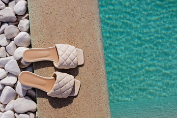 Stylish summer slippers on the edge on the swimming pool