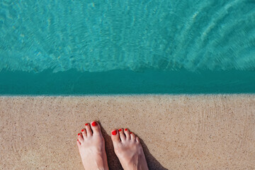 Fototapeta premium Feminine feet with red pedicure standing near the swimming pool