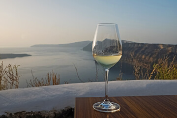 Glass of wine standing on the table with a view to Santorini caldera.