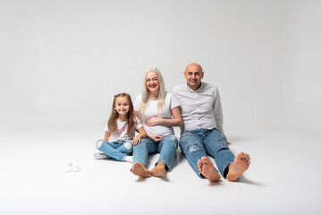 Happy family of three sitting on the floor, light background. Laughs: mother, father and little boy. Mom is pregnant. Good news, pregnant, bare feet to us