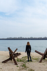 Ukrainian girl among anti-tank czech hedgehogs on river bank. Stop Russian military agression, war...