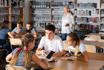 Cheerful teenage schoolboys and schoolgirls brainstorming in teams in library