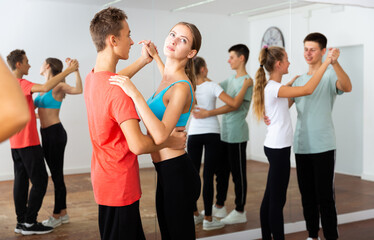 Teens in pairs learning to dance waltz with young female choreographer in modern studio ..