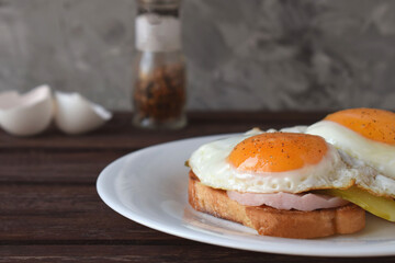 Fried eggs with liquid yolk on toasted bread with ham and pickles.