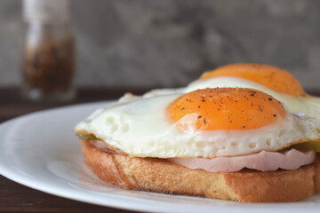 Fried eggs with liquid yolk on toasted bread with ham and pickles.