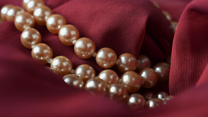 Women's necklace made of natural pearls on dark red chiffon fabric.