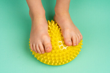 children's feet with a yellow balancer on a light green background, treatment and prevention of flat feet, valgus deformity of the foot - obrazy, fototapety, plakaty