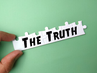 Hand holding white puzzle with text The Truth on green background.