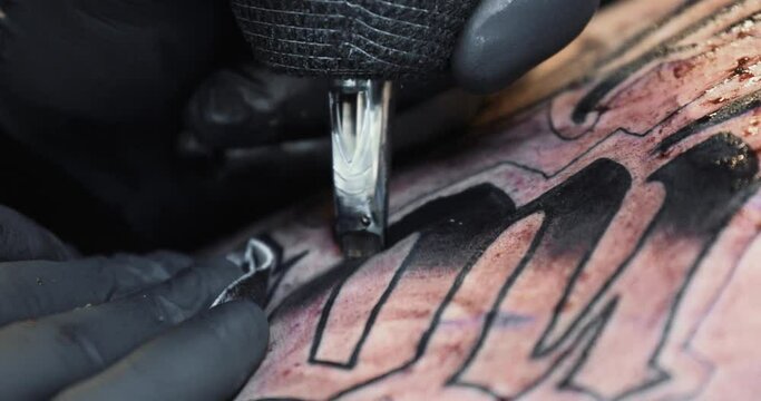 Close up of tattooing. Filling in large black lettering.Wiping off excess ink. Black latex gloves.
4K static shot.