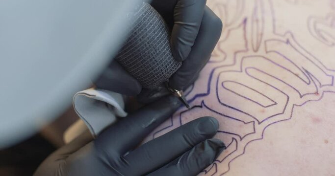 Tattooing an outline of lettering. Black latex gloves.
4K static shot.