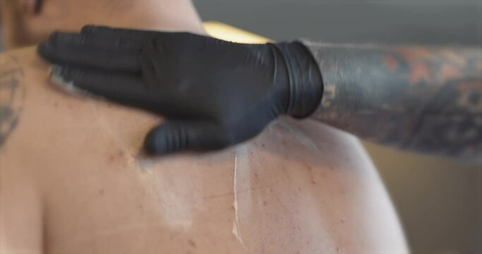Applying numbing cream to back and shoulders before tattoo. 
4K static shot.