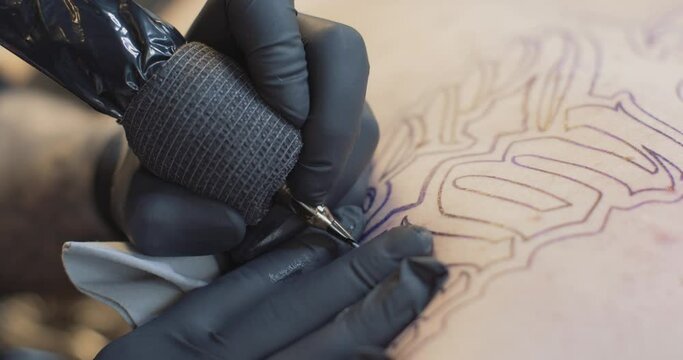 Close up of tattooing an outline of lettering. Black latex gloves.
4K static shot.