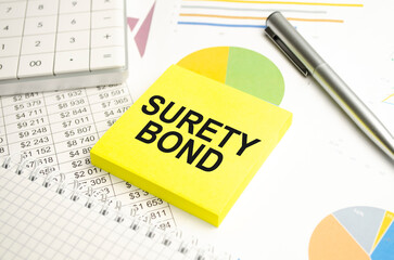 On the desktop there are reports, notepads, a calculator, a cash and a yellow sticker with the text SURETY BOND. Business concept