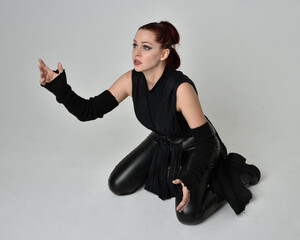 Full length portrait of pretty redhead female model wearing black futuristic scifi leather cloak...