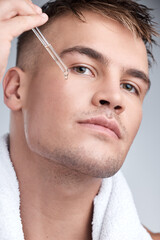 Beauty is unisex. Closeup shot of a young handsome man applying serum to his face against a grey...