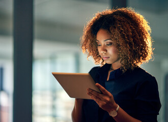 Working smart, working hard. Shot of a young businesswoman using a digital tablet during a late night at work. - Powered by Adobe