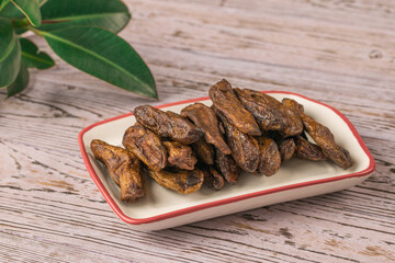 Dried bananas in a ceramic bowl and green leaves on a wooden table.