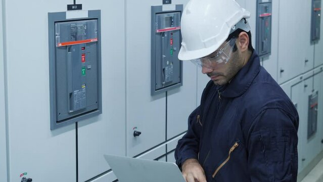 Electrical engineer using digital tablet inspect and program for electric power system in electrical control room. Engineer male working at factory. Concept of industry, factory, renewable energy.