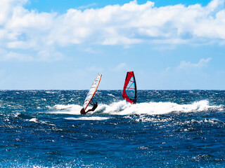 Two windsurfers blue water bright sun blue sky