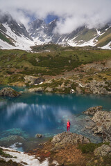 Hiking woman in red jacket standing at beautiful lake in mountains. - 499053716