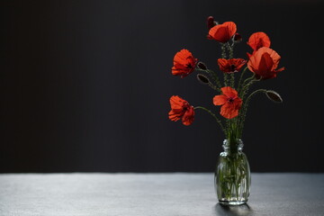 Glass bottle of red poppies stands on a black stone surface.