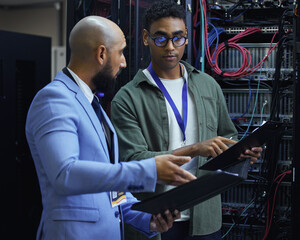 Going over the diagnostic report. Cropped shot of two male IT support agents working together in a dark network server room. - obrazy, fototapety, plakaty