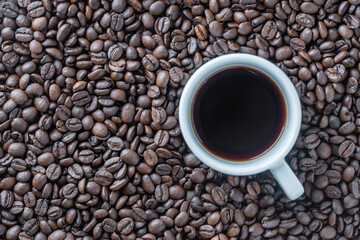 White cup of hot black coffee with a background of fresh roasted coffee beans, top view