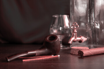 Moody smoking room with empty brandy glass and bottle and tobacco on the table. Vintage man's relaxation stuff