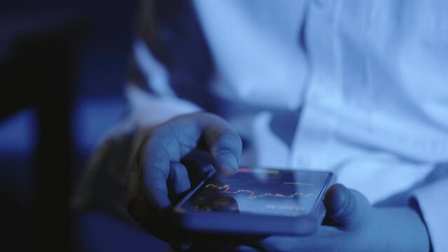 A close-up of a man's hand with a phone, the screen shows an online stock market chart showing bitcoin currencies. In blue light. In real time. Cryptocurrency. Investors