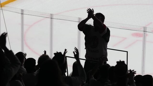 Silhouettes of sports fans with leader clapping hands to support hockey team players at competition on ice rink