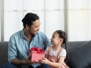 Handsome father and cute daughter looking at each other with love and happiness. Girl giving dad present for Father's day or birthday.