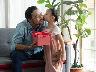 Cute daughter giving handsome dad a big kiss after giving present for special day. Father's day or Birthday concept. - obrazy, fototapety, plakaty