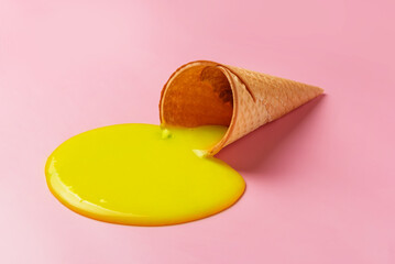 Melted ice cream flows out of a waffle cone on a pink background.