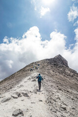 Obraz premium woman with backpack walking towards a group of hikers reaching the top of a mountain